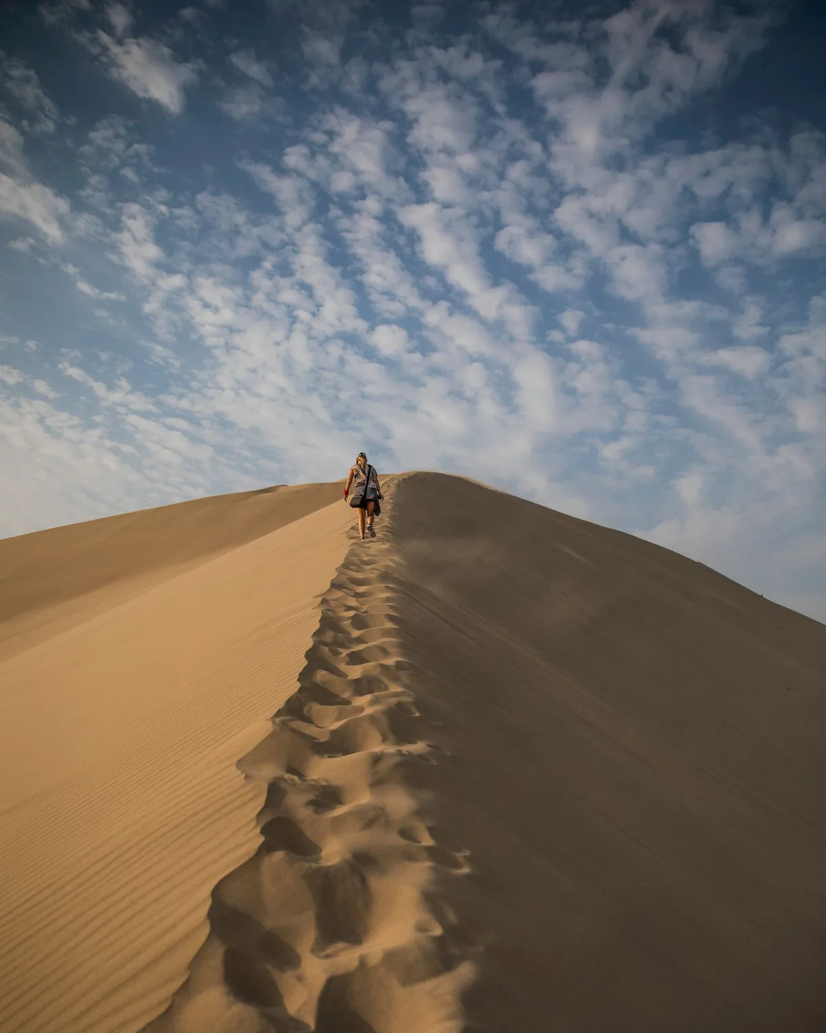 A person walking across the sand dunes of the Huacachina desert near Ica, Peru under a clear blue sky